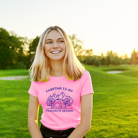  "Pink Graphic tee with an illustration of a tent, surrounded by nature. Text reads: 'Camping is my favorite season.' Celebrate the great outdoors!"